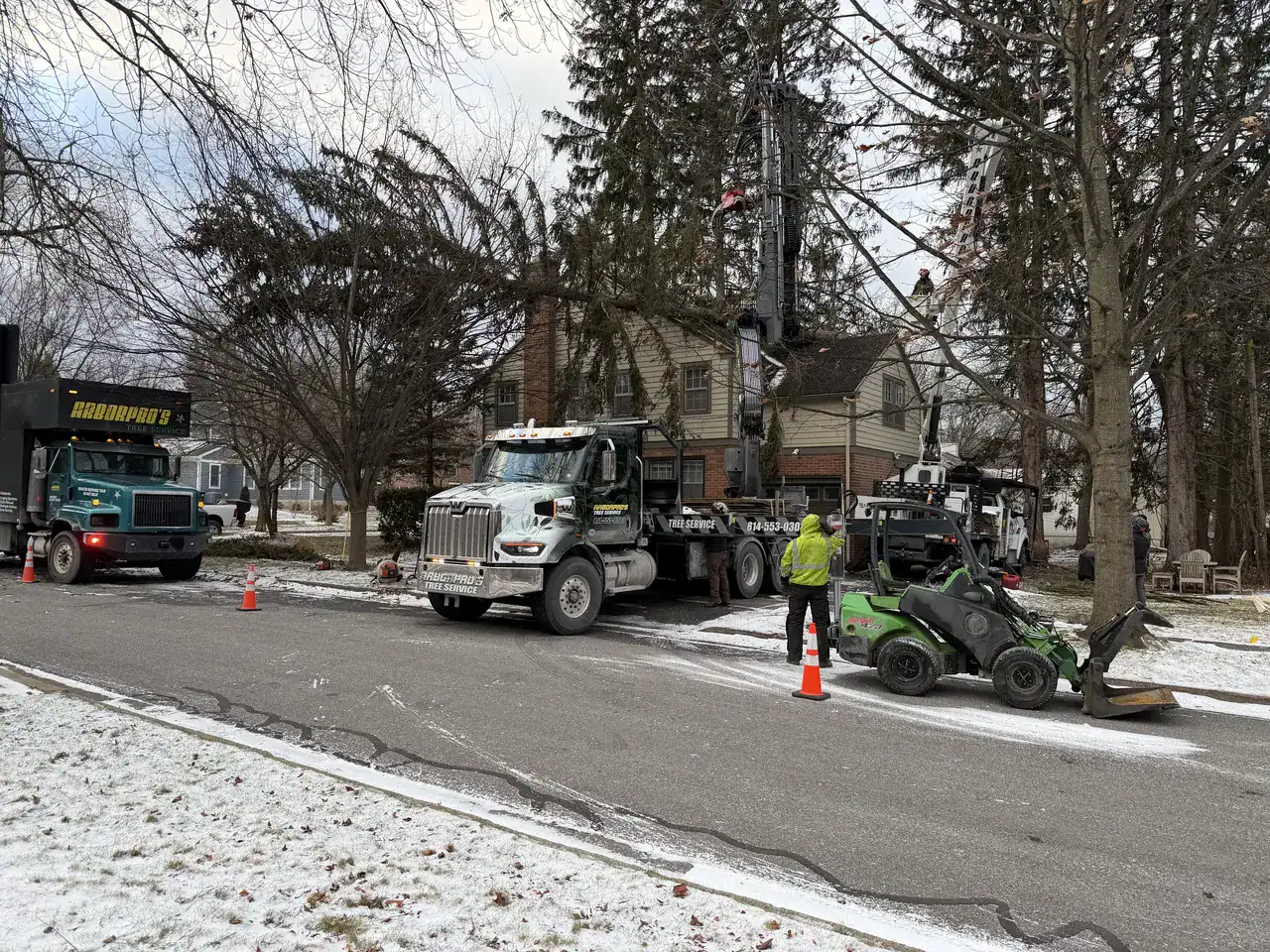 Crane boom lifting sections from a large conifer beside a house during winter tree removal in Central PA